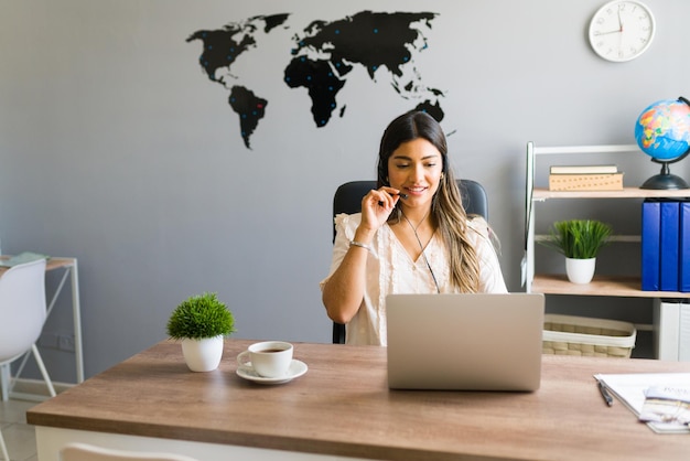 ¿Hola, como puedo ayudarte? Mujer joven hispana que trabaja en una agencia de viajes y habla con un cliente sobre reservar un vuelo para un viaje de negocios