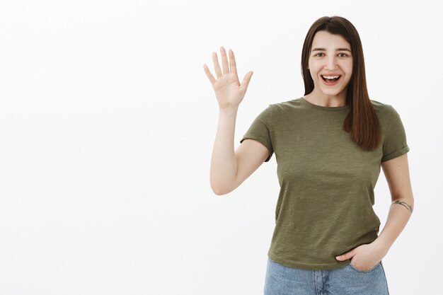 Hola, encantado de conocerte. Retrato de mujer saliente sincera amable y emocionada en camiseta diciendo hola como renuncia en gesto de hola y hola, saludando a los compañeros y sonriendo