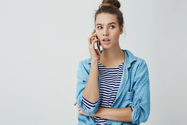 Hola puedo ordenar Retrato de linda mujer casual atractiva de moda mirando a un lado pensativo sosteniendo el teléfono inteligente presionado oído, hablando, reservando mesa restaurante a través del teléfono móvil