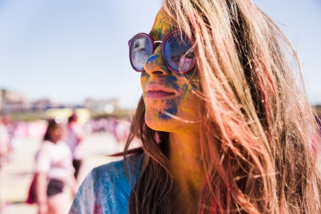 Holi colores sobre la cara de la mujer con gafas de sol