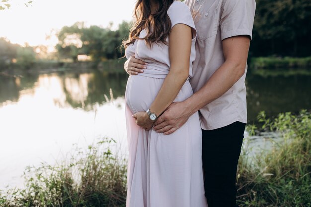 Hombre abraza hermosa mujer embarazada tierna de pie ante el lago