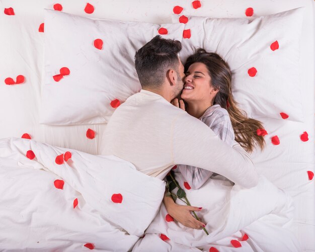 Hombre abrazando a mujer en la cama con pétalos de rosa