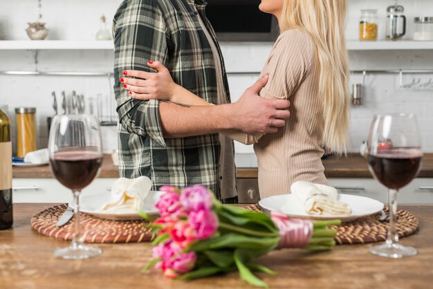 Hombre abrazando con mujer cerca de mesa con flores y copas de vino