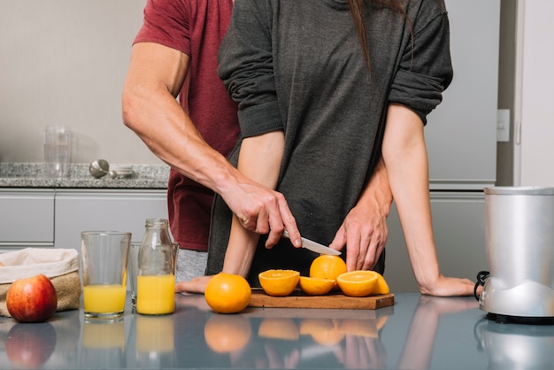 Hombre abrazando a la mujer por detrás y cortando naranja para jugo