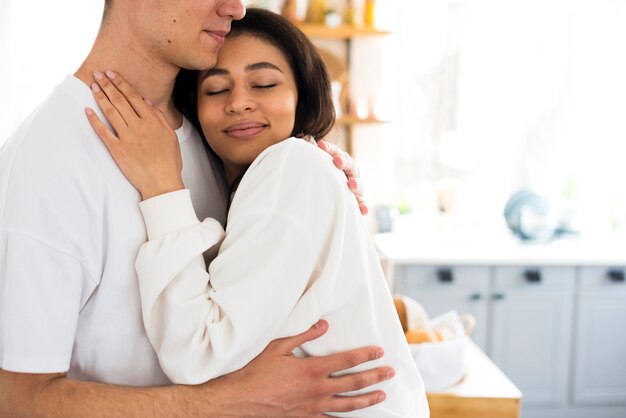 Hombre abrazando a la novia sonriente étnica con los ojos cerrados