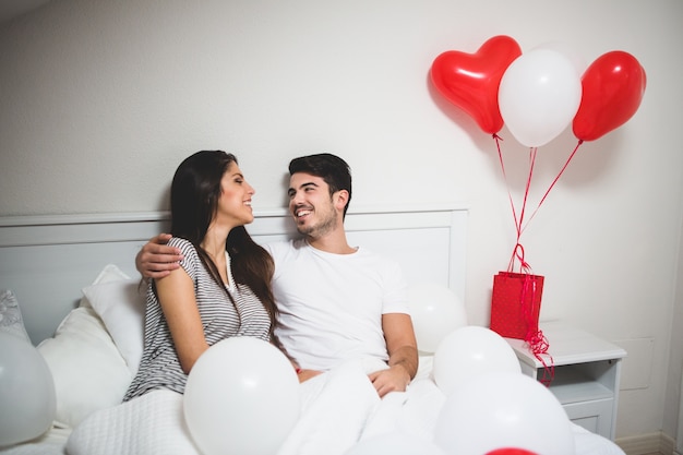 Hombre abrazando a su novia en la cama rodeados de globos