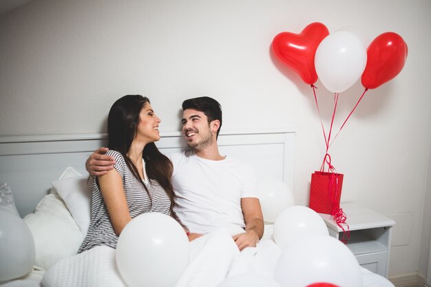 Hombre abrazando a su novia en la cama rodeados de globos