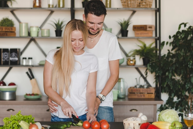 Hombre abrazando a su novia cortar verduras en el mostrador de la cocina