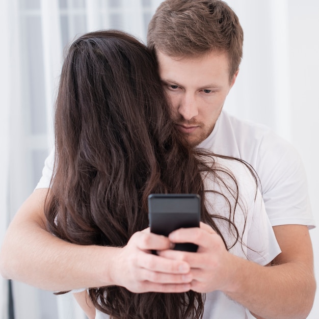 Hombre abrazando a su novia mientras revisa su teléfono