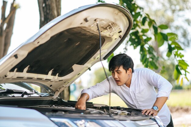 Un hombre abre el capó de un automóvil para reparar el automóvil debido a una avería.