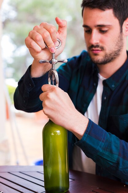 Hombre abriendo botella de alcohol con el abrelatas