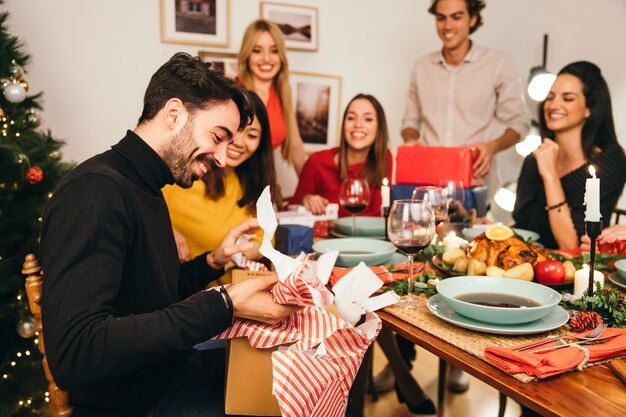 Hombre abriendo caja de regalo en cena de navidad