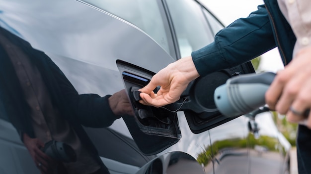 Hombre abriendo el enchufe de carga de los coches y sujetando el cargador en la estación de carga