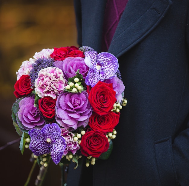 Hombre en abrigo con un ramo de flores mixtas rojo y púrpura.