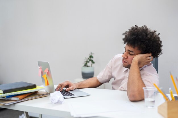 Hombre aburrido de tiro medio con computadora portátil en el trabajo