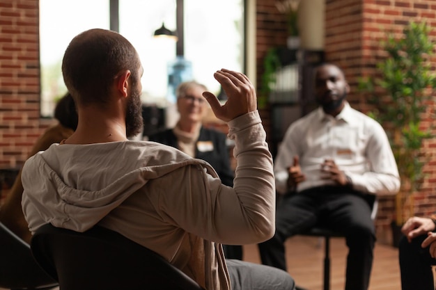 Hombre con adicción compartiendo problemas de salud mental con un grupo en una reunión, hablando con el terapeuta. Personas que conversan sobre la depresión y la rehabilitación en la sesión de terapia.