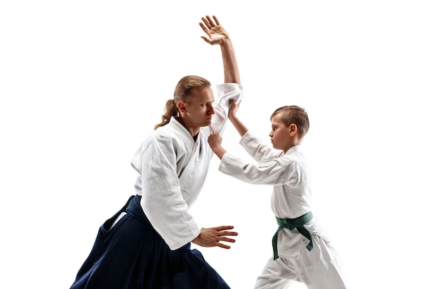 Hombre y adolescente peleando en el entrenamiento de Aikido en la escuela de artes marciales. Concepto de deporte y estilo de vida saludable. Fightrers en kimono blanco sobre pared blanca. Hombres de karate con caras concentradas en uniforme.