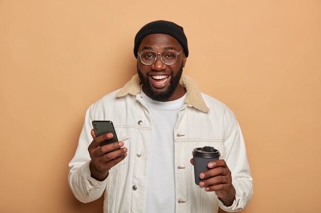 Hombre adulto sin afeitar negro con traje elegante, utiliza un teléfono inteligente moderno para chatear en línea