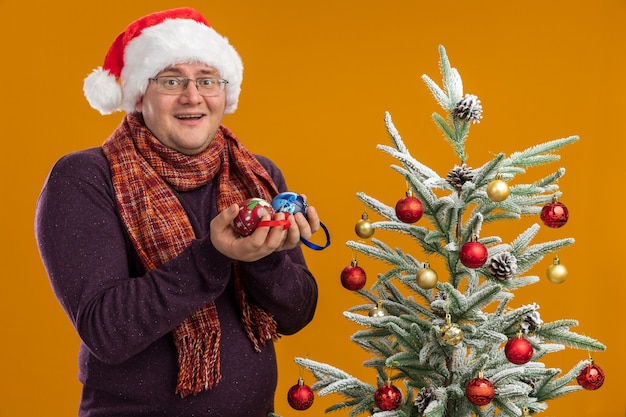 Hombre adulto alegre con gafas y gorro de Papá Noel con bufanda alrededor del cuello