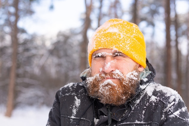 Un hombre adulto con barba en un bosque de invierno con toda la cara en la nieve, congelada, infeliz con el frío