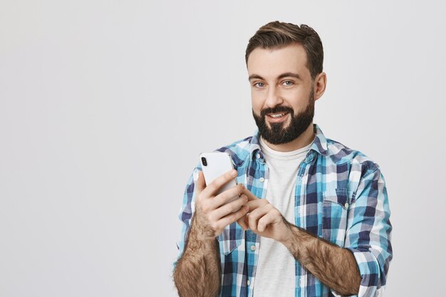 Hombre adulto con barba haciendo pedidos en línea mediante teléfono móvil