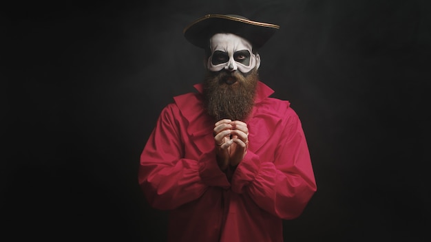 Hombre adulto con barba larga vestido como un capitán espeluznante sobre fondo negro.