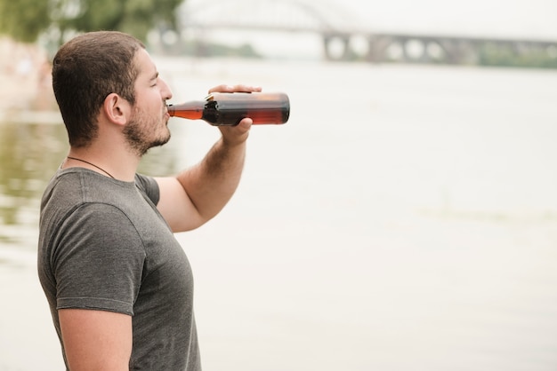 Hombre adulto bebiendo cerveza cerca del agua
