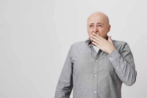 Hombre adulto calvo soñoliento agotado bostezando, cubrirse la cara y mirar a la izquierda