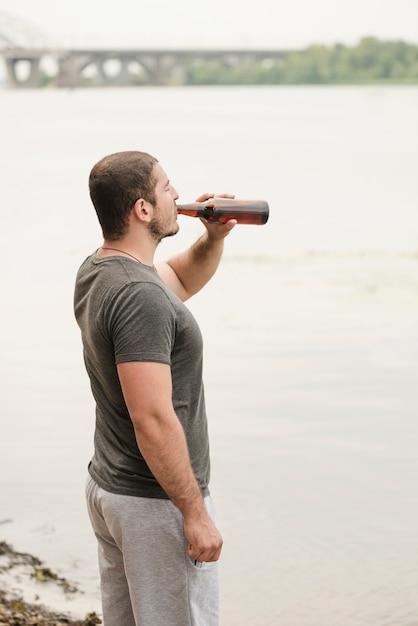 Hombre adulto disfrutando de cerveza cerca del río