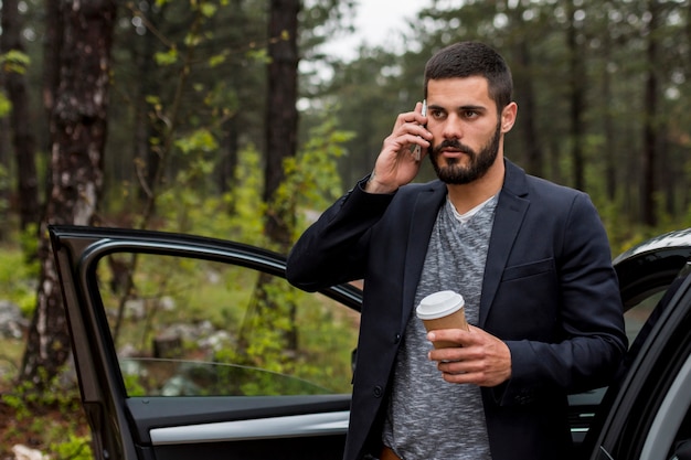 Hombre adulto hablando por teléfono cerca de la puerta del auto abierta