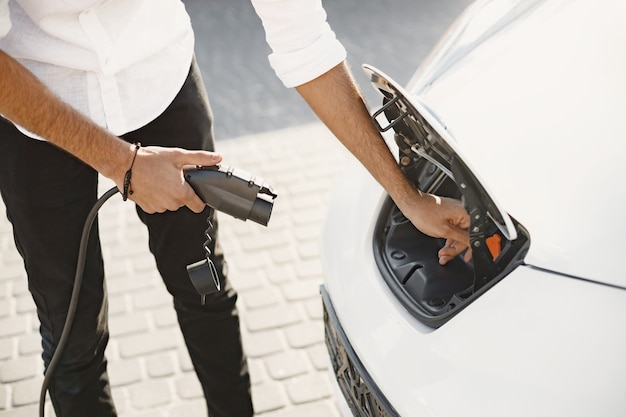 Hombre adulto joven cargando su coche eléctrico en la ciudad. Concepto de coche eléctrico ecológico.