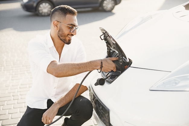 Hombre adulto joven cargando su coche eléctrico en la ciudad. Concepto de coche eléctrico ecológico.