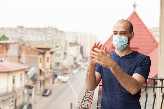 Hombre adulto con máscara de protección aplaudiendo en el balcón mostrando apoyo al personal médico en la lucha contra el coronavirus.