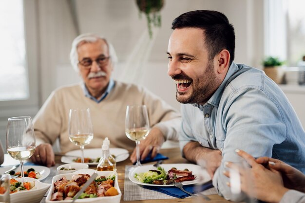 Hombre adulto medio feliz divirtiéndose durante el almuerzo familiar en la mesa de comedor