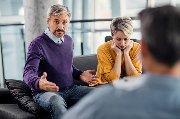 Hombre adulto medio hablando con un consejero matrimonial mientras está con su esposa en terapia de pareja