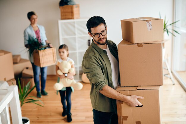 Hombre adulto medio que lleva una pila de cajas de cartón mientras se muda a un nuevo hogar con su familia