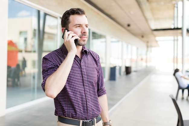 Foto gratuita hombre adulto medio tomando una llamada en el teléfono inteligente mientras está de pie en el centro comercial