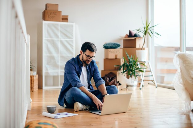 Hombre adulto medio usando una computadora portátil mientras está sentado en el suelo en su nuevo hogar