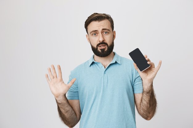 Hombre adulto nervioso levantar las manos y mostrando smartphone