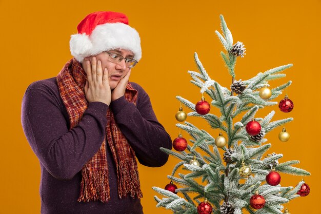 Hombre adulto preocupado con gafas y gorro de Papá Noel con bufanda alrededor del cuello
