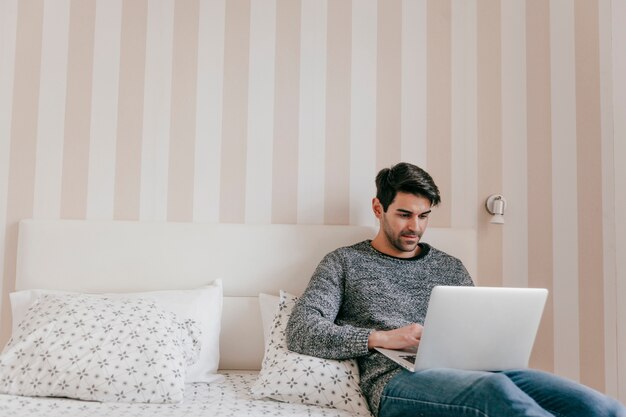 Hombre adulto que usa la computadora portátil en cama