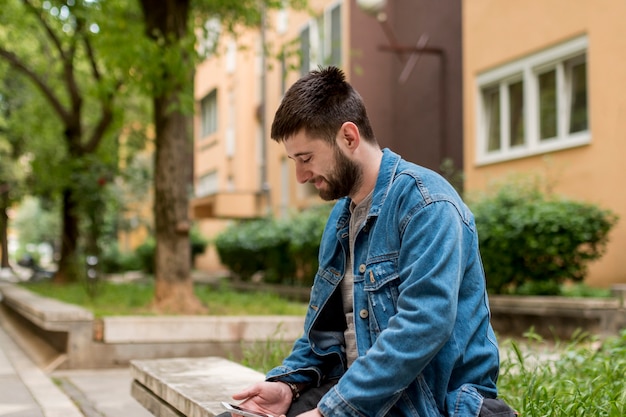 Hombre adulto sentado en un banco y usando un teléfono inteligente