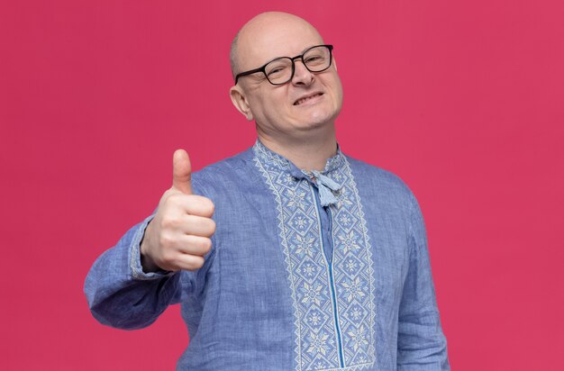 Hombre adulto sonriente en camisa azul con gafas pulgar hacia arriba