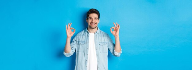Hombre adulto sonriente confiado que muestra señales de ok y parece complacido como algo que se opone a blu