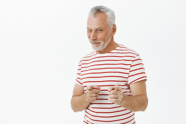 Hombre adulto sonriente descarado guiñando un ojo y señalando con el dedo