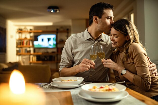 Hombre afectuoso besando a su novia mientras brinda con champán durante la cena en la mesa del comedor