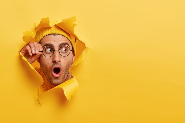 Hombre sin afeitar asombrado mira a través del agujero en papel amarillo