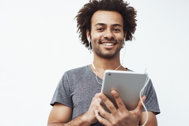 Hombre africano alegre en auriculares que sonríe sosteniendo la tableta.