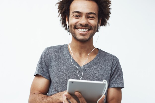 Hombre africano alegre en auriculares que sonríe sosteniendo la tableta.