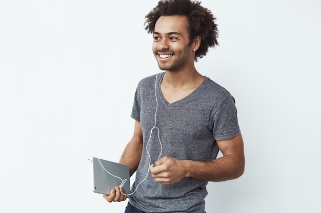 Foto gratuita hombre africano alegre en auriculares que sonríe sosteniendo la tableta.